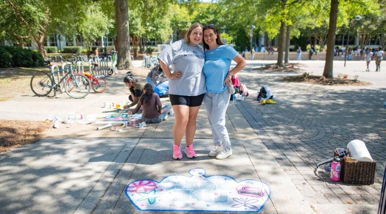 Two students pose for a photo on ODU's campus in front of a crown they painted on the sidewalk. 